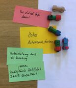 Auf dem Foto sind wenige beschriebene rote und grüne Moderationskarten zu sehen. Zwischen den Moderationskarten liegen Spielzeug-Lokomotiven und ein gelber Zettel mit der Aufschrift "Hohes Autonomiestreben".